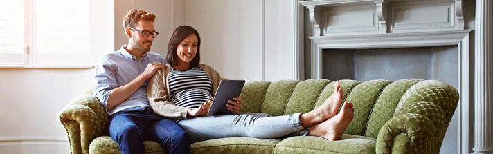 Pregnant couple sitting on a couch together looking at tablet