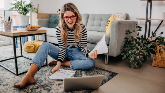 Woman sitting on her living room floor reviewing paperwork next to a laptop